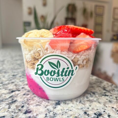 Pink and white bowl with granola, banana, and coconut shavings
